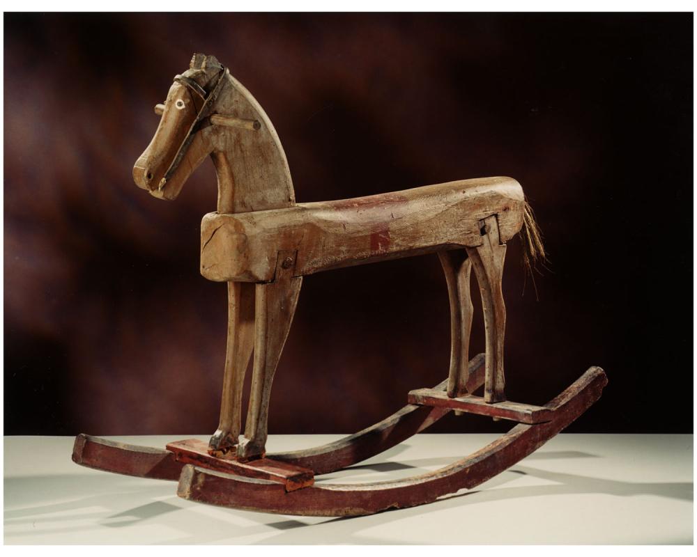 Cheval à bascule en bois. Des deux côtés de la tête se trouve une poignée, les yeux sont en relief et leur tour est peint en blanc, le filet rudimentaire a été réalisé en cuir, la selle et les sabots sont peints, la queue est en crin.