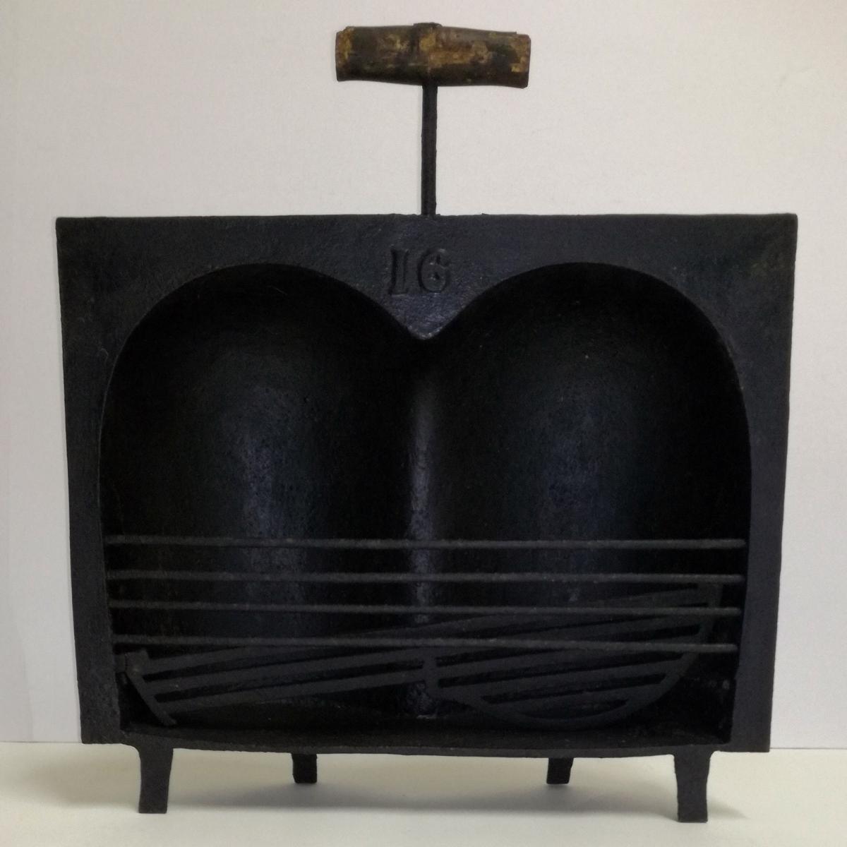 Coquille à rôtir en fonte avec une poignée en bois, surnommée "paire de fesses" en raison de sa forme.