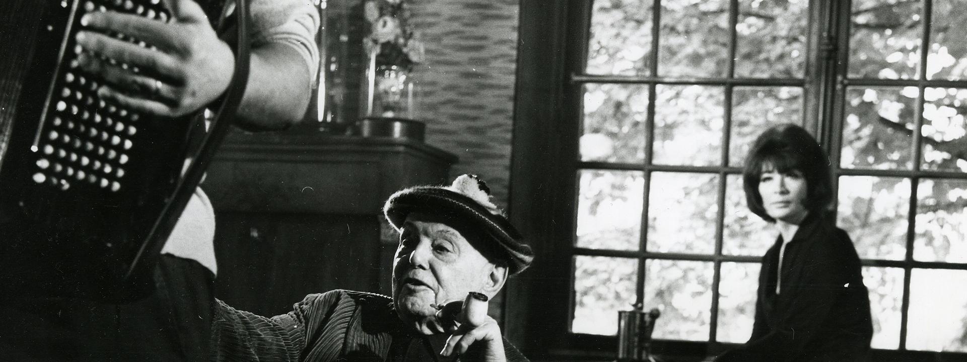 Juliette Gréco et Pierre Mac Orlan, dans la maison de l'écrivain à Saint Cyr-sur-Morin. Au premier plan un accordéoniste dont ne voit qu'un bras et une partie de l'accordéon