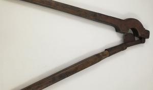 Photographie d'un coupe-queue, constitué de deux grandes branches. Une des branches est garnie d'un fourreau servant d'appui, dans laquelle s'encastre une lame tranchante en demi-lune, fixée à l'autre branche.