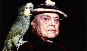 Photographie couleur représentant, sur un fond noir, un gros plan de l'écrivain Pierre Mac Orlan avec son perroquet posé sur l'épaule. Le perroquet est vert, Mac Orlan porte un béret.