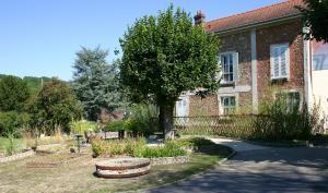 Meule en pierre, carrés de plantes utiles, tilleuls et barrière en osier devant l'entrée de la cour du Musée de la Seine-et-Marne.