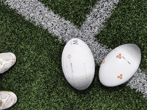 Deux ballons de rugby posés sur une ligne blanche tracée sur un terrain herbeux. Dans le coin en bas à gauche, le bout de deux chaussures de sport blanchesgauchesur 
