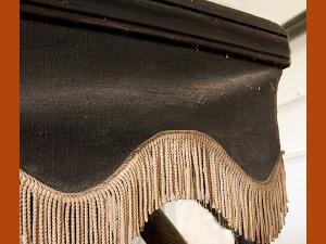 Détail d'une tenture du corbillard, en toile noire ornée d'un galon doré, dont l'éclat est estompé.