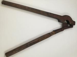 Photographie d'un coupe-queue, constitué de deux grandes branches. Une des branches est garnie d'un fourreau servant d'appui, dans laquelle s'encastre une lame tranchante en demi-lune, fixée à l'autre branche.