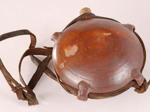 Gourde en grès, de forme sphérique, aux parois un peu aplaties, comportant une rainure sur le pourtour et des "passants" en grès pour permettre le passage d'un lien en cuir. La gourde est fermée par un bouchon de liège.