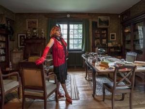 Scène de la visite théâtralisée "Les Marguerite de Mac Orlan" : Marguerite de la Nuit, vêtue à la mode des années 1930, se tient dans le bureau de la maison de Pierre Mac Orlan