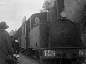Au début du 20ème siècle, un train entre en gare. Au 1er plan sur le quai, une femme vue de dos, coiffée d'un chapeau