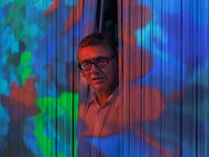 Portrait du plasticien Miguel Chevalier, il apparaît par l'ouverture de rideaux au milieu d'une œuvre projetée