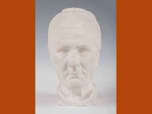 Sculpture en plâtre représentant la tête d'une vieille femme briarde ; ses traits sont marqués, ses cheveux plaqués en arrière par un bandeau.