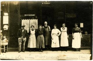 Photographie noir et blanc représentant la famille Guibert sur le seuil de leur café restaurant à Paris, entourés de leurs employés, dans les années 20