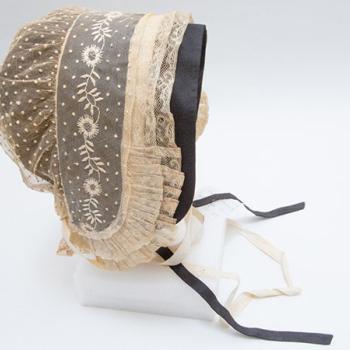 Coiffe en tulle de coton rebrodé de plumetis et de broderies blanches, volant de dentelle au fuseau orné de plis plats avec une sous coiffe de couleur noire.