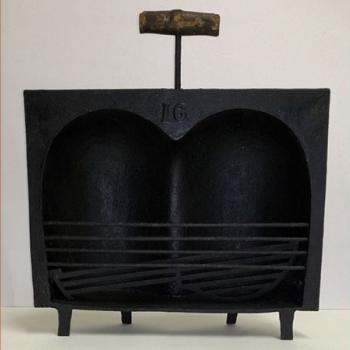 Coquille à rôtir en fonte avec une poignée en bois, surnommée "paire de fesses" en raison de sa forme.