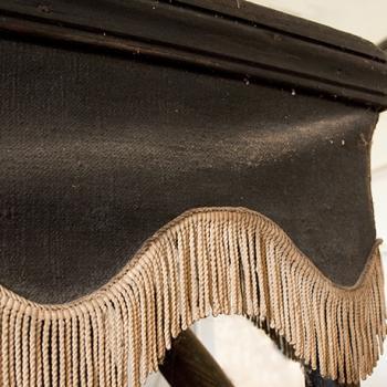 Détail d'une tenture du corbillard, en toile noire ornée d'un galon doré, dont l'éclat est estompé.