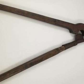 Photographie d'un coupe-queue, constitué de deux grandes branches. Une des branches est garnie d'un fourreau servant d'appui, dans laquelle s'encastre une lame tranchante en demi-lune, fixée à l'autre branche.