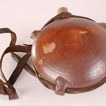 Gourde en grès, de forme sphérique, aux parois un peu aplaties, comportant une rainure sur le pourtour et des "passants" en grès pour permettre le passage d'un lien en cuir. La gourde est fermée par un bouchon de liège. 