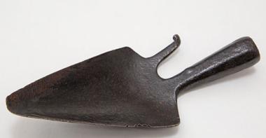 Outil en fer forgé, en forme de petite pelle pointue avec un crochet à droite. Le manche est manquant.