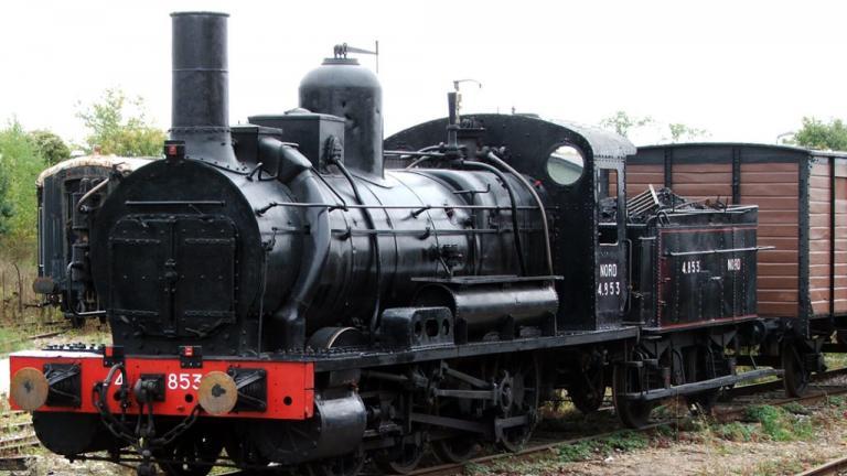 Photographie couleur d'une locomotive ancienne, avec une réserve de charbon et tirant un wagon de marchandises en bois