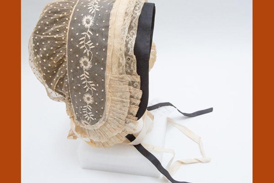 Coiffe en tulle de coton rebrodé de plumetis et de broderies blanches, volant de dentelle au fuseau orné de plis plats avec une sous coiffe de couleur noire.