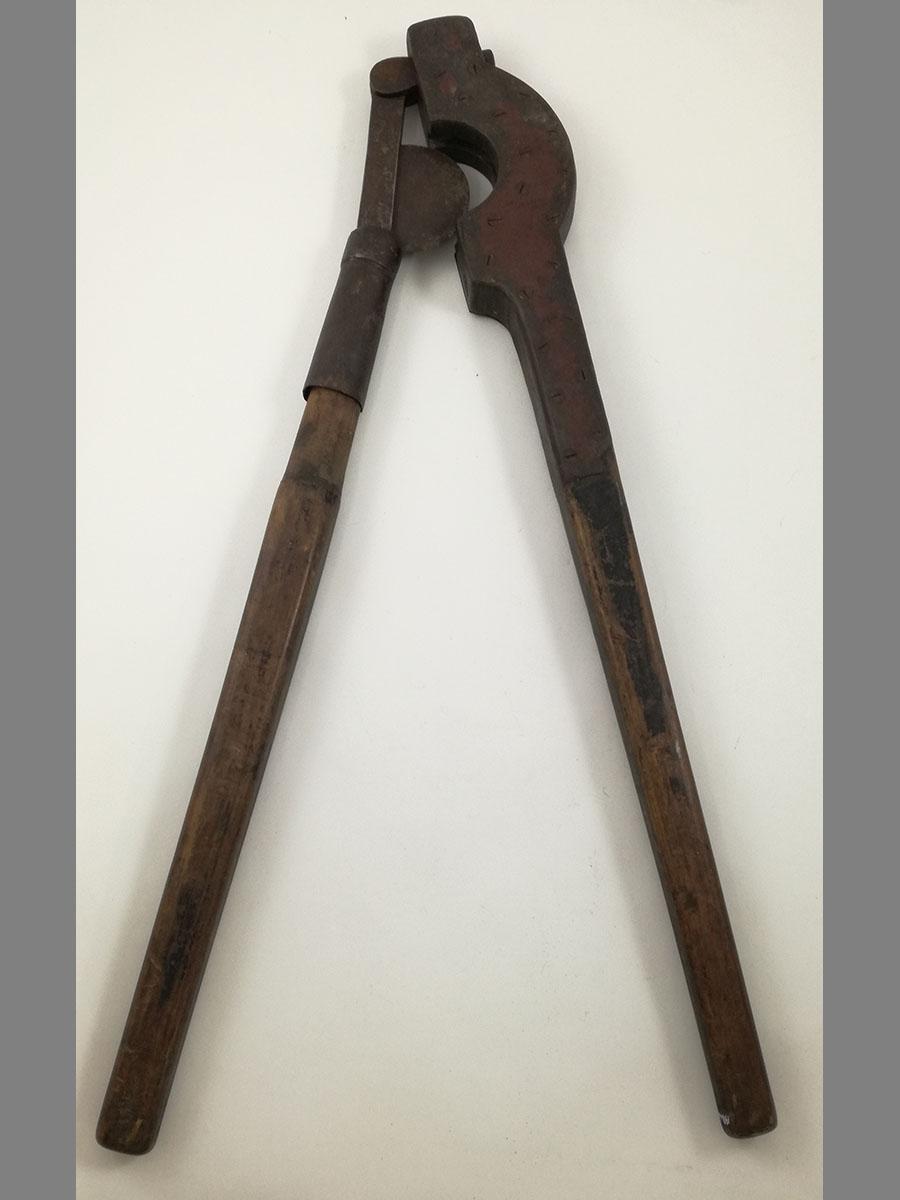 Photographie d'un coupe-queue, constitué de deux grandes branches. Une des branches est garnie d'un fourreau servant d'appui, dans laquelle s'encastre une lame tranchante en demi-lune, fixée à l'autre branche.