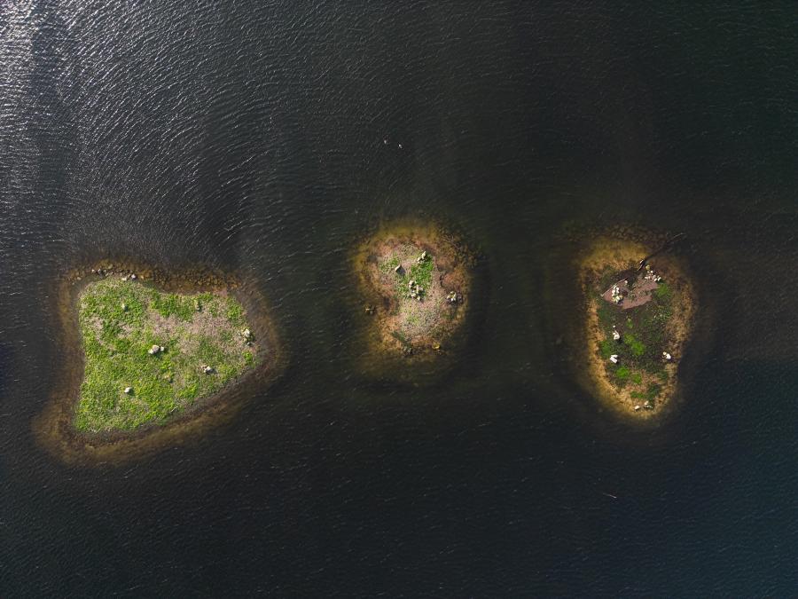 photographie aérienne de 3 îlots, de formes et tailles différentes, assez rapprochés, entourés d'une eau sombre.